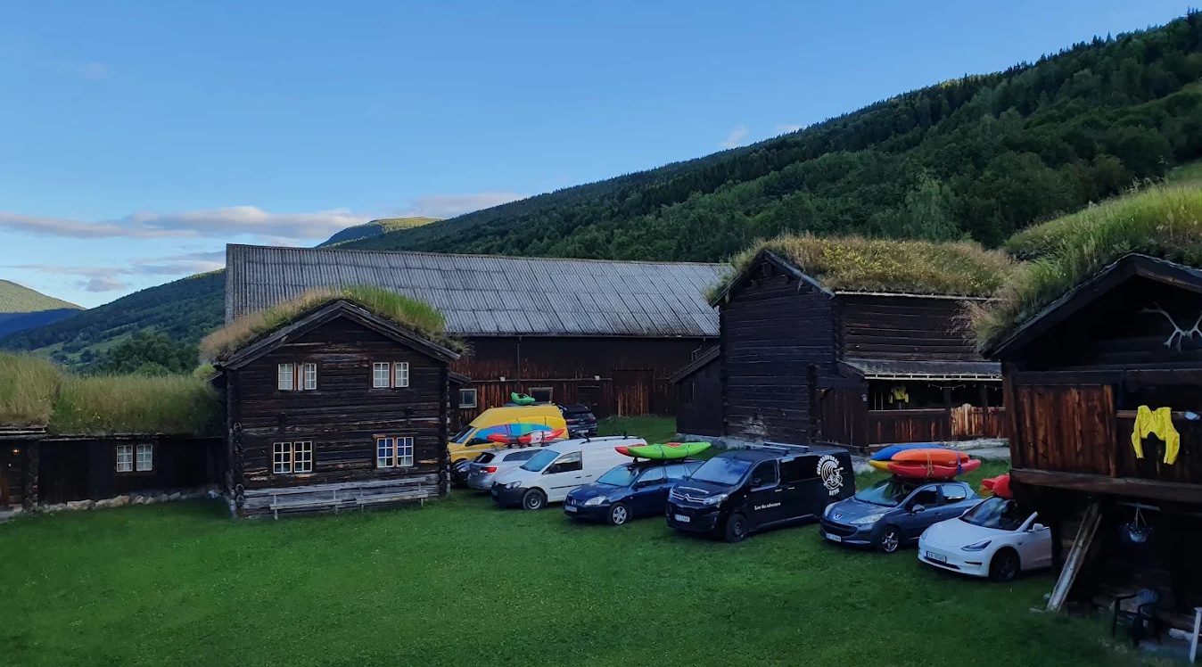 Kruke gård en sommerkveld, med biler og kajakker på takstativene foran tømmerhusene